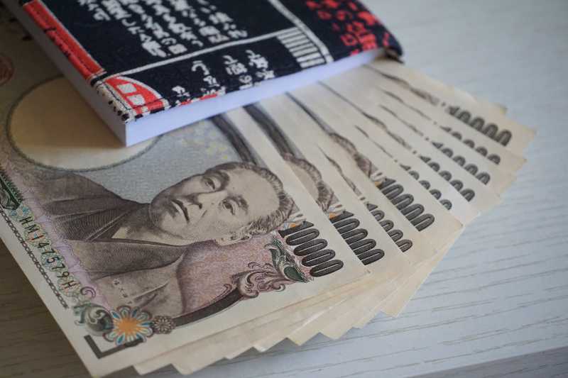 Japanese 10,000yen paper notes layed out on a table and pinned under a book.